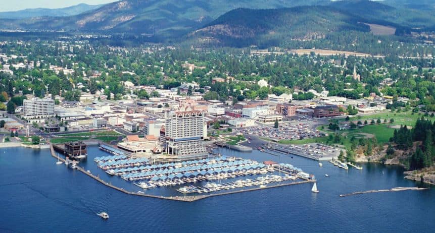 Aerial view of a waterfront city with marina and mountains in the background.