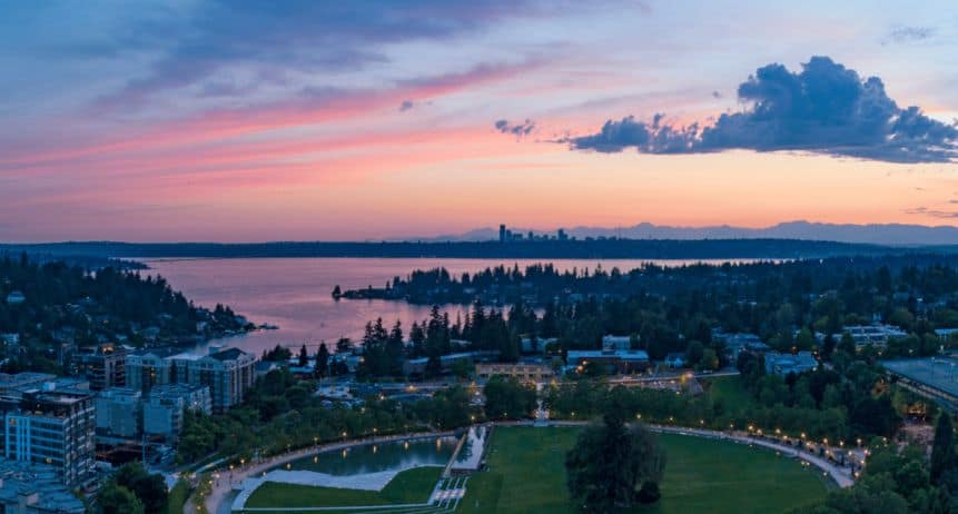 Aerial view of a city skyline during sunset with a river and lush green park in the foreground.