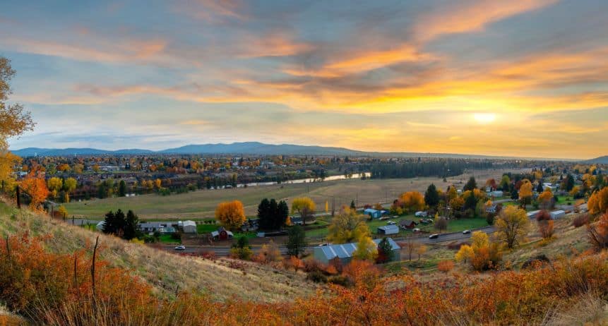 Scenic view of a rural landscape with houses, trees, and mountains at sunset.