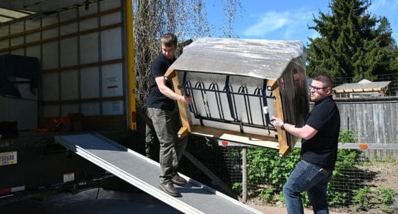 Two movers load a large furniture piece onto a truck for home delivery.