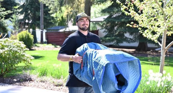 Professional mover with a large item in a lush outdoor setting.