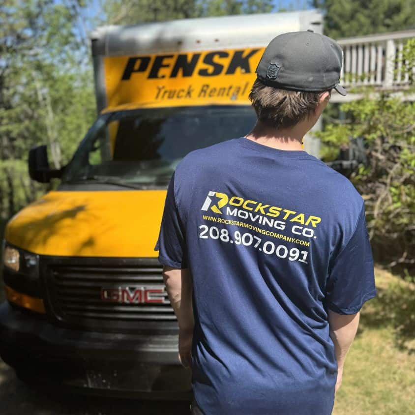 Moving company worker standing in front of a yellow Penske truck, wearing a Rockstar Moving shirt.