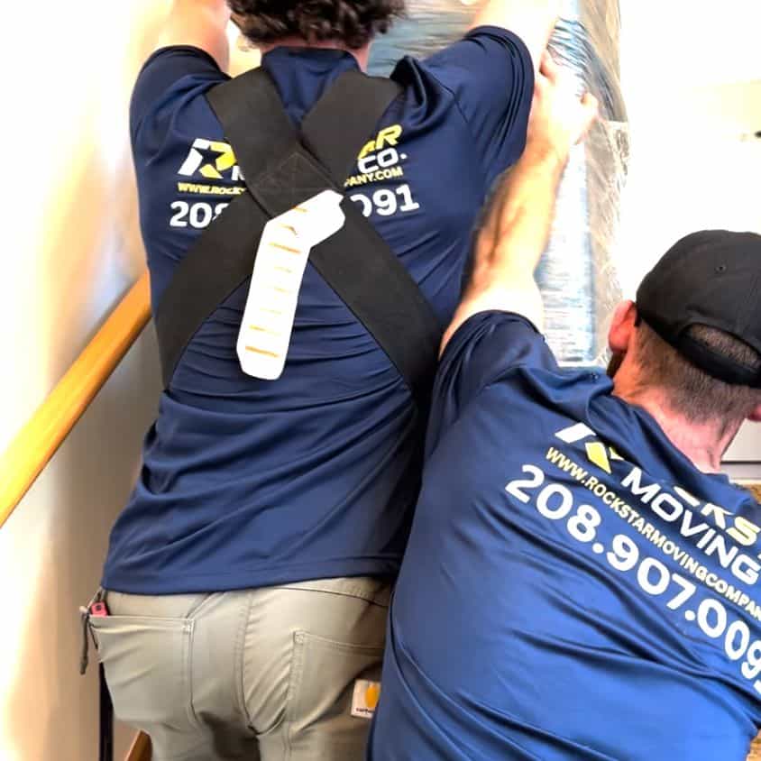 Two movers from Rockstar Moving Company lifting a large item up stairs.