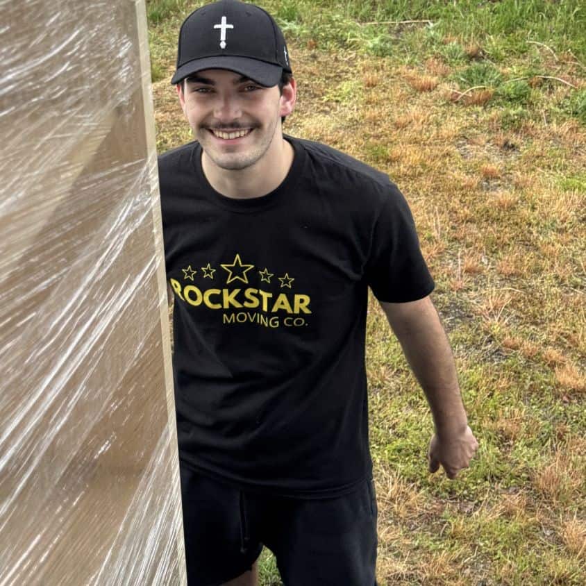 Moving company employee smiling outdoors with packed boxes.